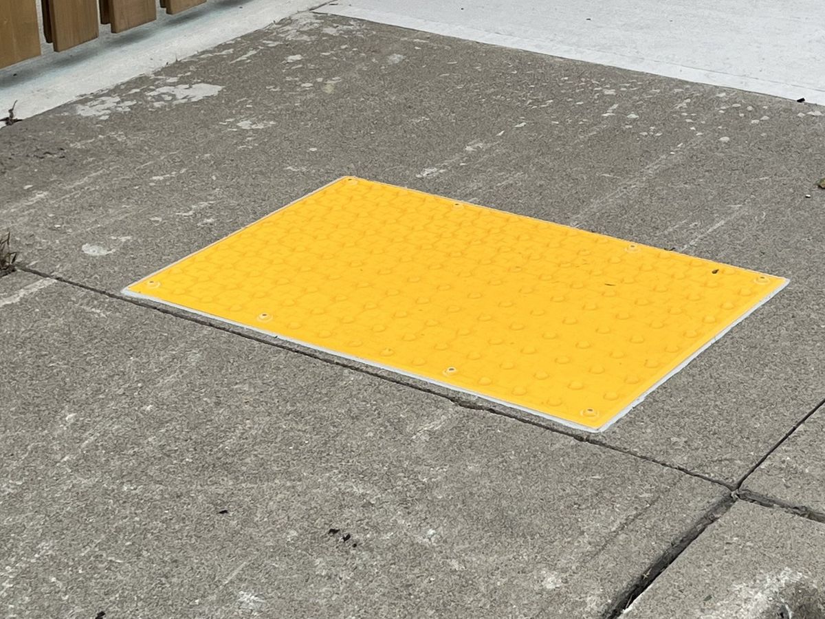 Yellow tactile access tile installed at the curb transition