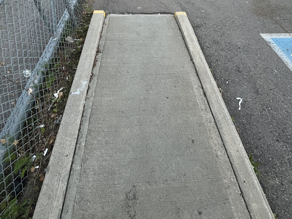 Narrow concrete walkway approach with no tactile indicator, before the retrofit